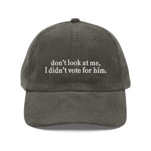 以下が含まれることがあります： オリーブグリーンのコーデュロイ野球帽。刺繍されたテキストは「don't look at me, I didn't vote for him.」つばはカーブしており、クラウンは丸みを帯びています。カジュアルなアクセサリーです。
