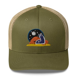 May include: A green and tan trucker hat with an embroidered design of a fox sitting under a crescent moon with stars. The fox is blue, orange, and yellow.