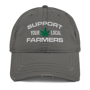 May include: A distressed gray baseball cap with the text "SUPPORT YOUR LOCAL FARMERS" embroidered in white. A green cannabis leaf is centered above the word "FARMERS". The cap has a curved brim and a worn appearance.