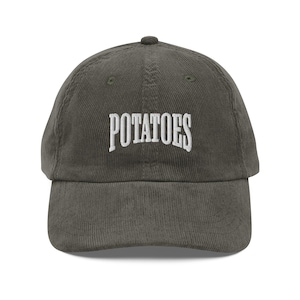 May include: A dark green corduroy baseball cap with the word "POTATOES" embroidered in white on the front.