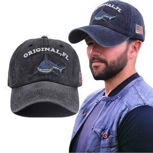 Puede incluir: Una gorra de béisbol negra desgastada con un tiburón bordado y el texto "ORIGINAL, FL" y una pequeña bandera estadounidense en el lateral.