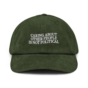 May include: Olive green corduroy baseball cap with the white text "CARING ABOUT OTHER PEOPLE IS NOT POLITICAL". The cap has a curved brim and an adjustable strap at the back.