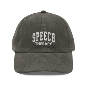 Può includere: Cappellino da baseball in velluto a coste verde oliva con la scritta bianca "SPEECH THERAPY". Il cappellino ha una visiera curva e un bottone sulla parte superiore. Un accessorio casual per logopedisti.
