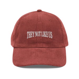 Könnte beinhalten: Eine rote Baseballkappe aus Cord mit weißer Stickerei, auf der "THEY NOT LIKE US" steht.