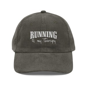 Puede incluir: Una gorra de béisbol de pana verde oscuro con bordado blanco que dice "RUNNING is my therapy".