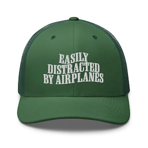 Peut inclure: Un chapeau de camionneur vert avec un message brodé en blanc qui dit "Easily Distracted By Airplanes".