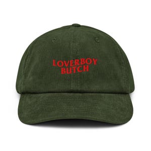 Könnte beinhalten: Grüne Cord-Baseballkappe mit dem gestickten Text "LOVERBOY BUTCH" in Rot. Die Kappe hat einen gebogenen Schirm und eine strukturierte Krone. Ein lässiges Accessoire.
