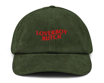 May include: A green corduroy baseball cap with the embroidered text "LOVERBOY BUTCH" in red. The cap has a curved brim and a structured crown. The hat is a casual accessory.
