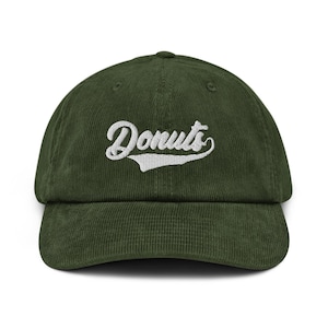 Könnte beinhalten: Grüne Cord-Baseballkappe mit dem Wort "Donuts" in weißer Schrift auf der Vorderseite gestickt. Die Kappe hat einen gebogenen Schirm und eine strukturierte Krone, geeignet für Freizeitkleidung.