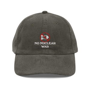 May include: Olive green corduroy baseball cap with the text "NO NUCLEAR WAR" embroidered in white. The design includes a red circle with a crossed-out missile symbol, promoting an anti-war message.