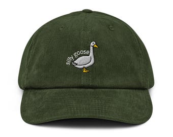 May include: A dark green corduroy baseball cap with the embroidered phrase "silly goose" and a cartoon goose illustration. The goose is white with a yellow beak and feet. The cap has a curved brim.