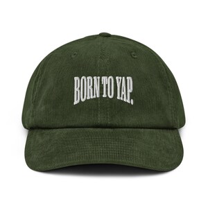 Peut inclure: Casquette de baseball en velours côtelé vert foncé avec le texte "BORN TO YAP" brodé en blanc sur le devant. La casquette a une visière incurvée et une sangle réglable à l'arrière.
