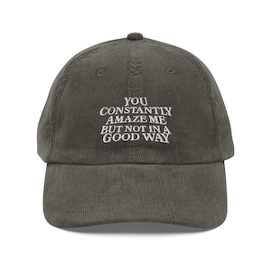Puede incluir: Gorra de béisbol de pana verde oliva con el texto bordado "YOU CONSTANTLY AMAZE ME BUT NOT IN A GOOD WAY". La gorra tiene una visera curva y una corona redondeada. Un accesorio casual.