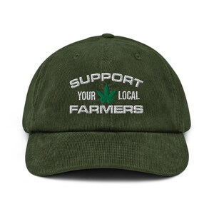May include: A dark green corduroy baseball cap with the text "SUPPORT YOUR LOCAL FARMERS" embroidered in white. A green cannabis leaf is centered between the words "YOUR" and "LOCAL". The cap has a curved brim and an adjustable strap.
