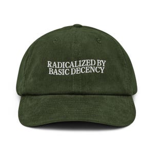 May include: A dark green corduroy baseball cap with the embroidered text "RADICALIZED BY BASIC DECENCY" in white. The cap has a curved brim and a structured crown, suitable for casual wear.