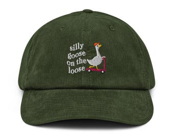 May include: A dark green corduroy baseball cap with the embroidered phrase "silly goose on the loose." The design features a cartoon goose riding a pink scooter, wearing an orange hat. The cap has a curved brim and a structured crown.