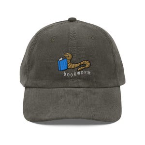 Op de afbeelding: Een donkergroene corduroy baseballpet met een geborduurd beeld van een worm die een boek leest en de tekst "bookworm".
