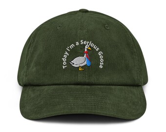 May include: A dark green corduroy baseball cap with the embroidered phrase "Today I'm a serious Goose" above a cartoon goose wearing a red tie and blue vest. The cap has a curved brim and a structured crown.