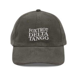 以下が含まれることがあります： 「FOXTROT DELTA TANGO」と白く刺繍された文字が入った、濃い緑色のコーデュロイ製のベースボールキャップです。