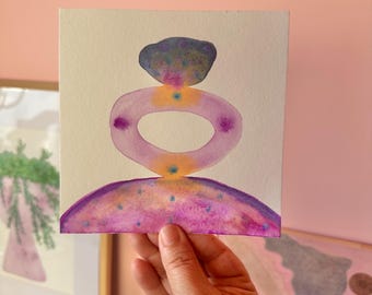 Könnte beinhalten: Ein quadratisches Aquarellbild auf weißem Papier mit drei gestapelten abstrakten Formen. Die obere Form ist ein dunkelvioletter Oval, die mittlere ein hellvioletter Ring und die untere ein violetter Halbkreis, alle mit gelben und blauen Akzenten.