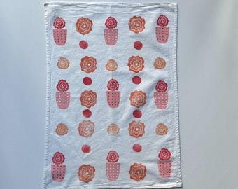 Könnte beinhalten: Weißes Küchentuch mit einem sich wiederholenden Muster aus rosa und orangefarbenen Blumen in Töpfen. Die Blumen sind stilisiert und haben ein einfaches Design.