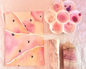 Könnte beinhalten: Draufsicht auf ein Aquarell in Rosa- und Pfirsichtönen, eine blütenförmige Farbpalette mit rosa Farbe und zwei Kristalltürmen. Das Gemälde hat schwarze Punkte und weiße Linien. Die Kristalle sind rosa und lila.