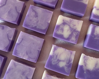 Könnte beinhalten: Eine Ansammlung von quadratischen Seifenstücken, die in einem Raster angeordnet sind. Jedes Stück weist ein marmoriertes Design mit Wirbeln aus tiefem Violett und cremigen Weißtönen auf. Die Seifenstücke haben eine glatte, feste Textur.