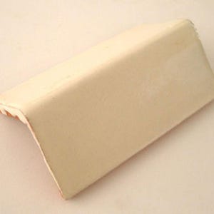 May include: A cream-colored, right-angled corner molding piece. The molding has a smooth, matte finish and a beveled edge. The corner piece is designed to protect and decorate the corner of a wall or other surface.