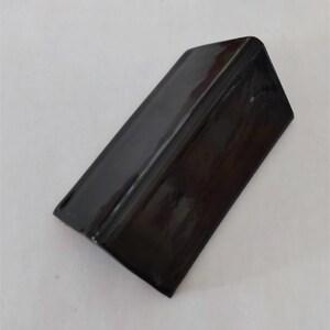 May include: A glossy, black, rectangular object with a rounded corner. The object appears to be made of a solid material and has a reflective surface. The item is set against a plain, light background.