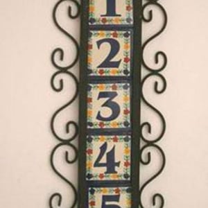 May include: Vertical address plaque with numbers 1 through 5. Each number is on a square tile with a floral border. The tiles are set in a black metal frame with decorative scrollwork.