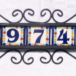 May include: Decorative address plaque featuring the numbers 69742. The numbers are in a bold blue font on individual tiles with a floral design. The tiles are set in a black wrought iron frame with decorative scrollwork.