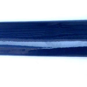 May include: A rectangular, navy blue ceramic tile with a glossy finish. The tile has a rounded edge and a visible wood grain texture. The end of the tile is a reddish-brown color. The tile is approximately 1 inch wide.