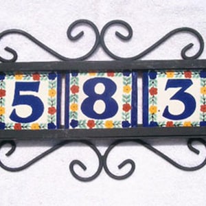 May include: Decorative address plaque featuring the numbers 583 on three ceramic tiles. The tiles have a floral design with blue, red, yellow, and green accents. The plaque is framed by a black wrought iron scroll design.