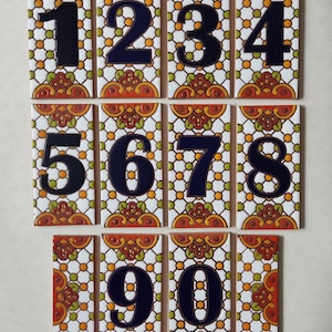 May include: A collection of ten rectangular ceramic tiles, each displaying a different number from zero to nine. The numbers are in a dark blue, bold font. The tiles have a decorative pattern with orange, green, and white floral designs.