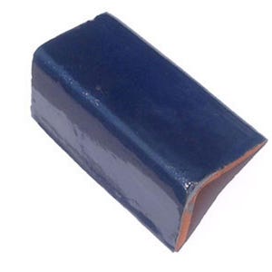 May include: A rectangular, glazed, dark blue ceramic tile with a rounded corner. The tile has a glossy finish and a visible edge of unglazed, reddish-brown clay. The shape suggests it may be a decorative trim piece.