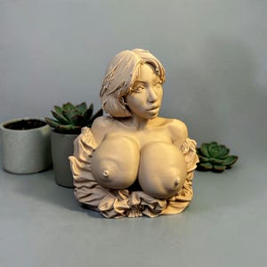 May include: A beige-colored 3D printed bust sculpture of a person with short hair, wearing an off-the-shoulder garment with ruffled detailing. The sculpture features a smooth, matte finish and is rendered in a monochromatic light tan tone.