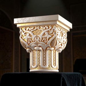 May include: An intricately carved architectural column capital in cream and gold. The design features detailed floral and geometric patterns. The capital has a square top and is displayed on a dark surface. The overall aesthetic is one of elegance and detail.