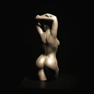 Op de afbeelding: Sepia-getinte sculptuur van een torso, armen boven het hoofd geheven. De rug heeft een gedetailleerde wervelkolom en decoratieve patronen. De sculptuur staat tegen een donkere achtergrond, die de vorm benadrukt.