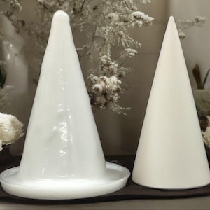 May include: Two white ceramic cone-shaped candle holders. The holder on the left has a wider base and a textured surface. The holder on the right has a smooth surface.