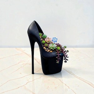 Puede incluir: Una maceta con forma de zapato de tacón alto en color negro mate que contiene una variedad de pequeñas suculentas verdes y moradas, guijarros y un pequeño letrero azul con el texto "Aura's Garden" insertado en la tierra.