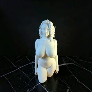 May include: A matte white 3D printed figurine of a person with curly hair, depicted from the waist up. The figure is shown in a standing pose, wearing only a simple bikini bottom, with detailed facial features and a realistic body shape.