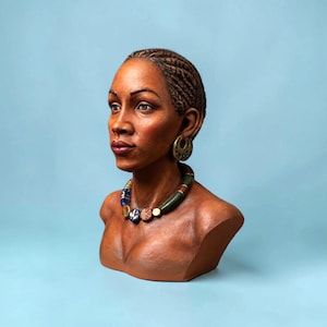 Pode incluir: Um busto esculpido de uma pessoa com cabelo trançado, usando grandes brincos de argola dourados e um colar de contas com peças cilíndricas e circulares em azul, verde e com padrões. A escultura tem um acabamento castanho quente e traços.
