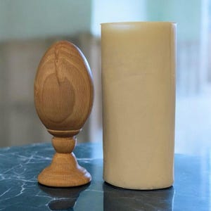 May include: A wooden egg-shaped object with a base, sitting on a blue marble surface next to a tall, cream-coloured cylinder.