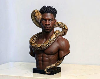 May include: A detailed sculpture bust of a dark-skinned person with short, textured hair, featuring a large, patterned brown and tan snake coiled around the neck and shoulders. The figure is shirtless, showing defined chest and abdominal muscles.