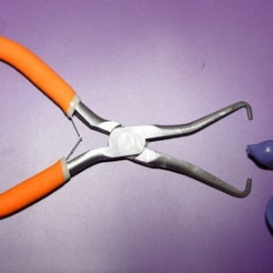 May include: Orange handled pliers with silver metal jaws and a purple glass sea turtle with a blue and white floral design.