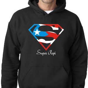 May include: Black hooded sweatshirt with a red, white, and blue Superman logo with the Puerto Rican flag colors. The text "Super Papi" is printed below the logo.