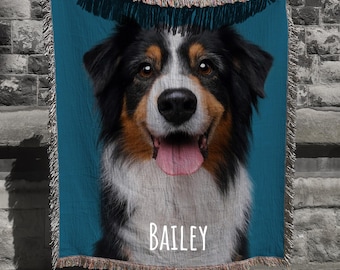 May include: A woven throw blanket featuring a close-up of a dog's face with black, brown, and white fur, a pink tongue, and the name "BAILEY" in white text. The background is teal, and the blanket has a fringed edge.