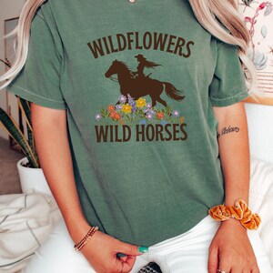 May include: A green t-shirt with the text "Wildflowers Wild Horses" and a silhouette of a woman riding a horse with flowers around the horse.