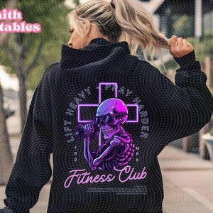 May include: Black hoodie with a neon purple and pink graphic of a skeleton lifting weights, wearing sunglasses, and a cross. Text includes "LIFT HEAVY, PRAY HARDER" and "Fitness Club". The words "Faith Printables" are in the top left.