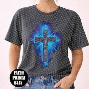 May include: Dark gray t-shirt featuring a vibrant, blue and purple cross design with a cosmic background. The cross incorporates elements resembling a game controller. The shirt also has the text "FAITH PRINTABLES" in a black circle.